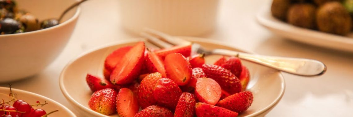 Close-up of fresh strawberries in a bowl with spoons, surrounded by various dishes.